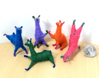 May include: A collection of five colorful felted llama figurines in various poses. The llamas are blue, green, purple, orange, and pink, with contrasting colored legs and ears. A US quarter is included for size reference.