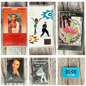 May include: A collection of vintage cassette tapes featuring album art. The tapes include artists like Whitney Houston, Bob Marley, and Vanilla Ice. The album covers showcase portraits and graphic designs, with vibrant colors and text.