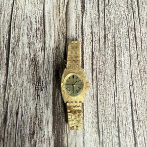 May include: A vintage gold-toned wristwatch with a rectangular face and a textured band. The watch has a light green face with gold hands and markers. The band is made of small, connected gold links.