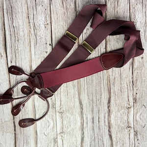 Puede incluir: Tirantes burdeos con ajustadores de metal dorado y detalles de cuero. Los tirantes tienen un diseño en forma de Y con enganches de cuero. Las correas elásticas son de color burdeos oscuro.