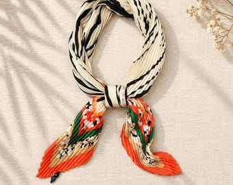 Könnte beinhalten: Ein plissiertes Halstuch mit einem cremefarbenen und schwarzen Zebramuster an der oberen Schlaufe, das in einen lebendigen unteren Bereich mit orangefarbenen, grünen und weißen Blumenmotiven übergeht. Der Stoff hat eine ausgeprägte Akkordeon-Faltenstruktur.