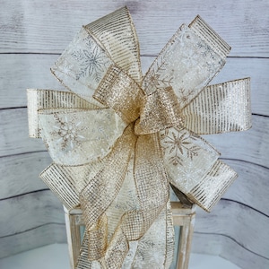 May include: A gold and white ribbon bow with snowflake patterns, tied around a wooden lantern.