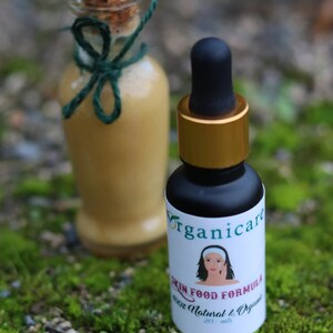 May include: Two glass bottles with labels. The smaller bottle is a dark amber color with a gold lid and a dropper. The label says "Organicare Skin Food Formula 100% Natural & Organic 20 ml". The larger bottle is clear with a cork stopper and a green ribbon. The background is green moss.