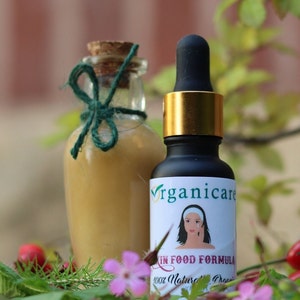 May include: Two glass bottles with labels. The bottle on the left is clear and has a green ribbon tied around the neck. The bottle on the right is dark brown and has a gold lid with a dropper. The label on the bottle on the right says "Organicare Skin Food Formula 100% Natural Organic".