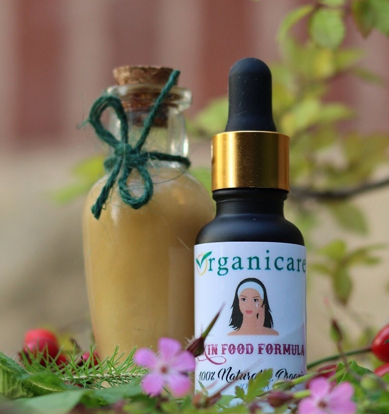 May include: Two glass bottles with labels. The bottle on the left is clear and has a green ribbon tied around the neck. The bottle on the right is dark brown and has a gold lid with a dropper. The label on the bottle on the right says "Organicare Skin Food Formula 100% Natural Organic".