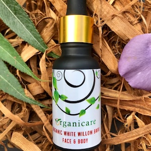 Puede incluir: Un pequeño frasco de vidrio negro con tapa dorada y gotero. El frasco está etiquetado con "Organicare Organic White Willow Bark Face & Body".