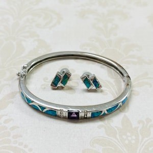 May include: Silver-toned bracelet and matching earrings set. The bracelet features turquoise and blue inlay with a rectangular purple stone. The earrings have a geometric design with turquoise and blue inlay. A stylish jewelry set.