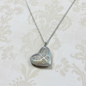 May include: A silver-toned heart-shaped pendant necklace. The pendant features a butterfly design embellished with clear crystals. The necklace chain is a delicate, woven style. The background is a floral pattern.