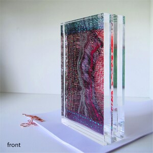 May include: A multi-layered clear acrylic block with a colorful fabric design inside. The fabric is a mix of red, purple, blue, and white with a glittery texture.