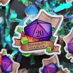 Könnte beinhalten: Ein Aufkleber mit einem violetten und blauen 20-seitigen Würfel mit einem Galaxie-Design. Der Würfel ist von grünen Kristallen und einem Banner mit der Aufschrift "Dungeon Master" umgeben.