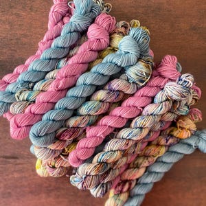 Könnte beinhalten: Eine Sammlung bunter Garnknäuel in den Farben Rosa, Blau und Gelb. Das Garn ist zu einem Stapel angeordnet, wobei die Enden der Knäuel sichtbar sind.