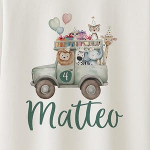 May include: White t-shirt with a colorful graphic of a safari truck carrying party animals, balloons, and gifts. The number 4 and the name "Matteo" are also displayed on the shirt.