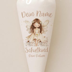 May include: A white, cone-shaped school cone with a tied top. The cone features a watercolor illustration of a fairy with the text "Dein Name" above the fairy and "Schulkind" below. The text "Bügelbild" is at the top.