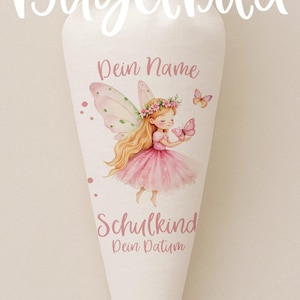 Pode incluir: Saco escolar branco em forma de cone com uma ilustração de fada. A fada tem cabelo loiro, um vestido rosa e asas de borboleta. A bolsa tem o texto "Bügelbild", "Dein Name", "Schulkind" e "Dein Datum".