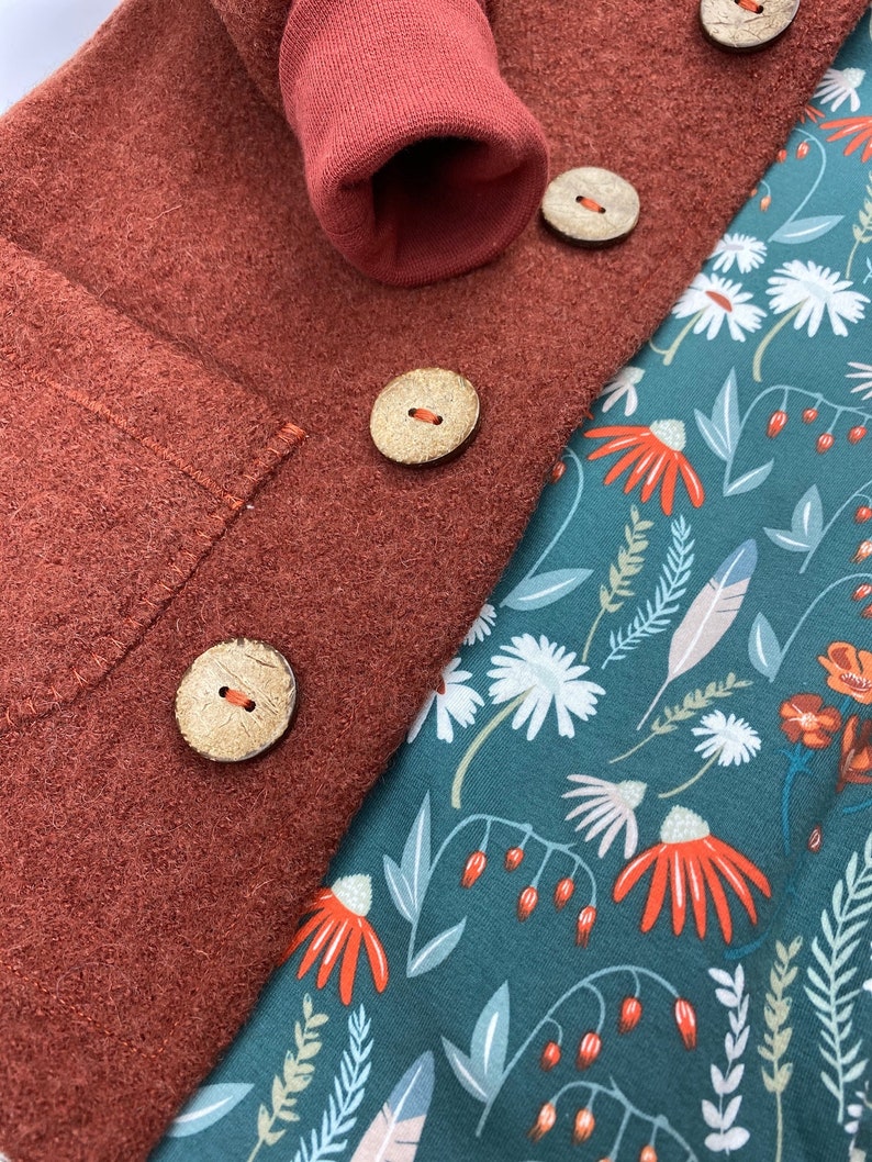 May include: A close-up of a rust-coloured fabric with three wooden buttons. The fabric is folded over a teal fabric with a floral pattern.