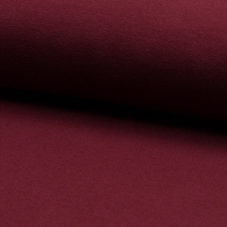 May include: Close-up of a deep burgundy fabric with a smooth, slightly textured surface.