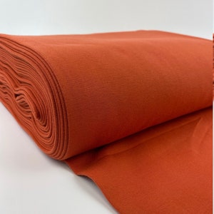 May include: A roll of rust-colored fabric, folded and displayed on a white surface.