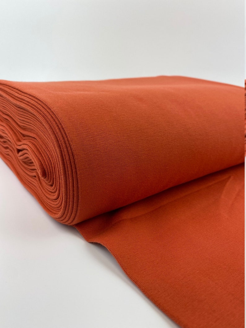 May include: A roll of rust-colored fabric, folded and displayed on a white surface.