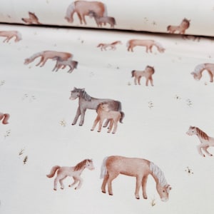 May include: Cream-colored fabric featuring a repeating pattern of watercolor-style horses and foals in various poses. The horses are depicted in shades of brown and gray, with some grazing and others standing. Small green plants are scattered across the background.