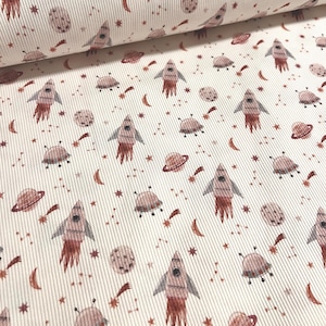 Può includere: Tessuto bianco con un motivo ripetuto di razzi rosa e arancioni, pianeti, stelle e stelle cadenti. Il tessuto ha una texture a coste.