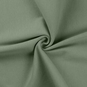 May include: A solid sage green fabric with a smooth, uniform texture. The material is gathered in the center, creating soft, flowing folds and deep shadows that highlight the consistent matte finish and the muted, earthy tone of the textile.