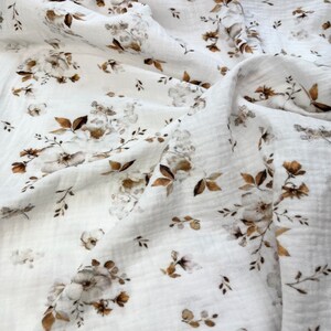 Puede incluir: Tela blanca con un patr&oacute;n floral marr&oacute;n. La tela es suave y tiene una textura arrugada.