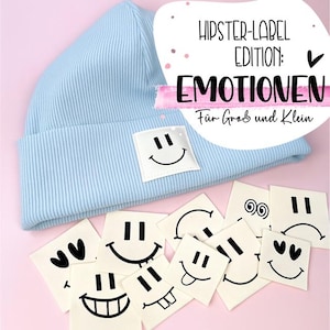 Può includere: Un berretto blu chiaro a coste con un'applicazione quadrata bianca con una faccina sorridente. Sotto ci sono diversi piccoli quadrati bianchi con diversi disegni di faccine sorridenti. Il testo sull'immagine recita: "HIPSTER-LABEL EDITION: EMOTIONEN".