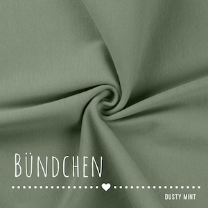 May include: A solid dusty mint green fabric with a smooth, fine-knit texture featuring soft folds and ripples. The text B&Uuml;NDCHEN is printed in white in the lower left corner, followed by a dotted line with a heart and the text DUSTY MINT.