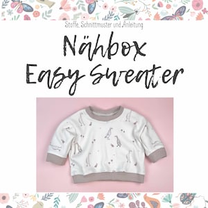 Può includere: Una felpa bianca con un bordo marrone e un motivo di oche su uno sfondo rosa. Il testo "Nähbox Easy Sweater" è scritto sopra la felpa.