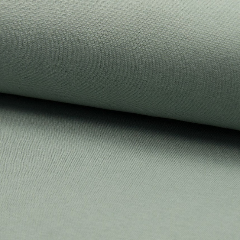 Puede incluir: Primer plano de una tela suave de color verde salvia con una textura sutil. La tela es lisa y parece ser un tejido de punto.