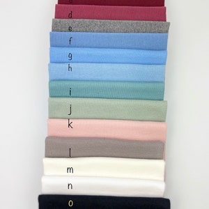 May include: A stack of 15 fabric swatches in various colors, including mustard yellow, red, burgundy, pink, gray, blue, and black. The swatches are labeled with letters from a to o.