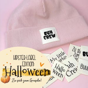 Pode incluir: Um gorro rosa claro canelado com uma etiqueta branca que diz "BUH CREW". Várias etiquetas brancas pequenas com texto estão espalhadas ao redor do chapéu. A imagem também inclui o texto "HIPSTER-LABEL EDITION: Halloween" e "Zu süß zum Gruseln!"