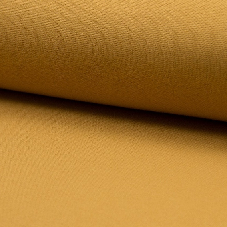 May include: A close-up of a roll of mustard yellow fabric. The fabric has a soft, textured surface.