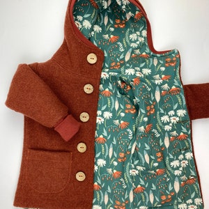 May include: A rust-coloured hooded jacket with a floral print lining. The jacket has a pocket on the front and wooden buttons.