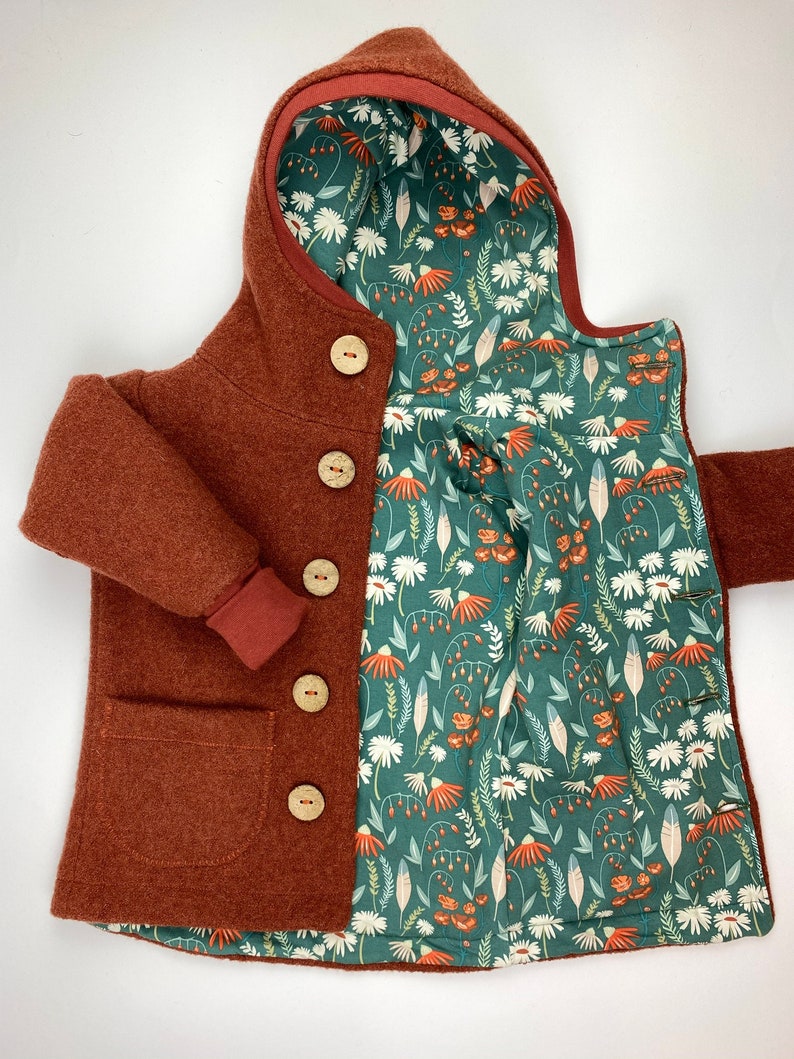May include: A rust-coloured hooded jacket with a floral print lining. The jacket has a pocket on the front and wooden buttons.