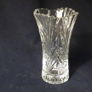 May include: A clear glass vase with a scalloped rim and a cut-glass design. The vase is tall and slender, with a wide base.