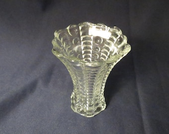May include: A clear glass vase with a flared, scalloped rim. The vase has a textured pattern of vertical lines and small circles. The vase is likely vintage and suitable for small floral arrangements or decorative display.