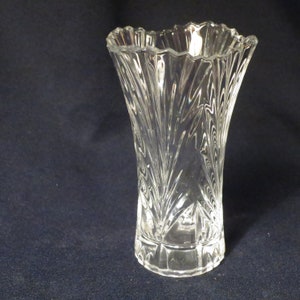 May include: A clear glass vase with a fluted design. The vase has a wide mouth and a narrow base.