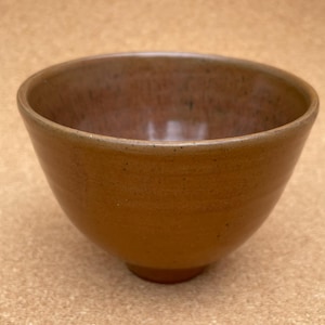 May include: A brown ceramic bowl with a slightly flared rim. The bowl has a smooth, slightly textured surface.