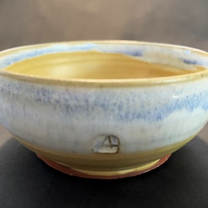Peut inclure: Un petit bol rond en céramique avec un intérieur jaune clair et un extérieur blanc avec un glaçage bleu. Le bol a un bord brun et une base brune.