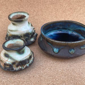 May include: Three ceramic pottery pieces, two small white vases with brown and blue glaze and a larger bowl with a blue and brown glaze.