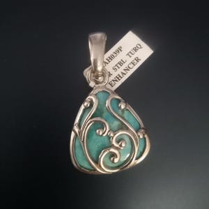 May include: A teardrop-shaped pendant with a turquoise stone and a silver filigree design. The pendant has a bail at the top for a chain. The tag reads "AH039P R STBL TURQ ENHANCER".