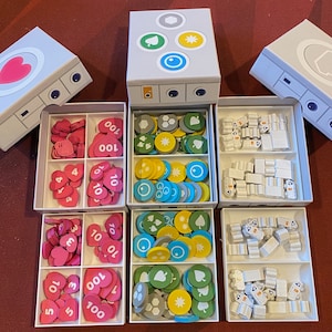 Op de afbeelding: Een set van zes witte opbergdozen met deksels. Elke doos bevat verschillende gekleurde fiches met nummers en symbolen. De dozen zijn gerangschikt in twee rijen van drie. De deksels zijn open om de inhoud te laten zien.