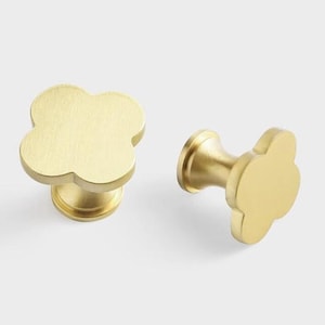 May include: Two gold-toned metal cabinet knobs with a four-leaf clover design. The knobs have a smooth, brushed finish.
