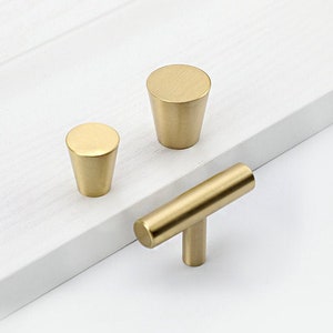 May include: Three gold cabinet knobs, two are round and one is a T-shaped pull.