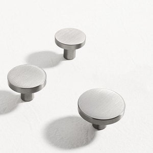 May include: Three silver round cabinet knobs with a brushed finish. The knobs have a circular base and a short, cylindrical stem.