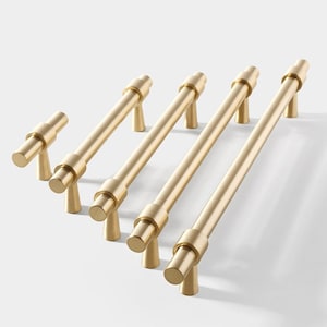 May include: Five gold-toned cabinet pulls with a simple, modern design. The pulls are all the same length and have a rounded, cylindrical shape.