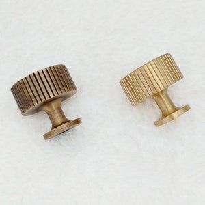 May include: Two brass cabinet knobs with a fluted design. The knobs have a round top and a cylindrical base.