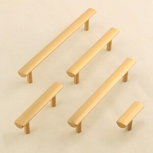 May include: Five gold cabinet pulls in various sizes. The pulls are all rectangular with rounded edges and a single screw hole.