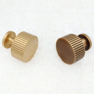 May include: Two brass cabinet knobs with a ribbed design. The knobs are round and have a smooth, polished finish.